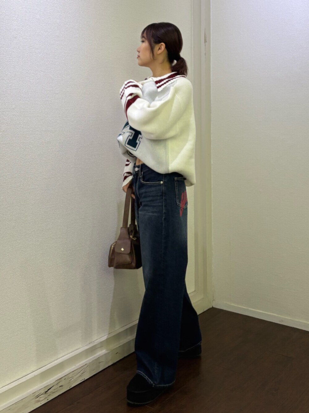 ブルー系のデニムパンツ、ブラウン系のハンドバッグ、ホワイト系のニット/セーターを着用したレディースの冬コーディネートの2枚目の写真