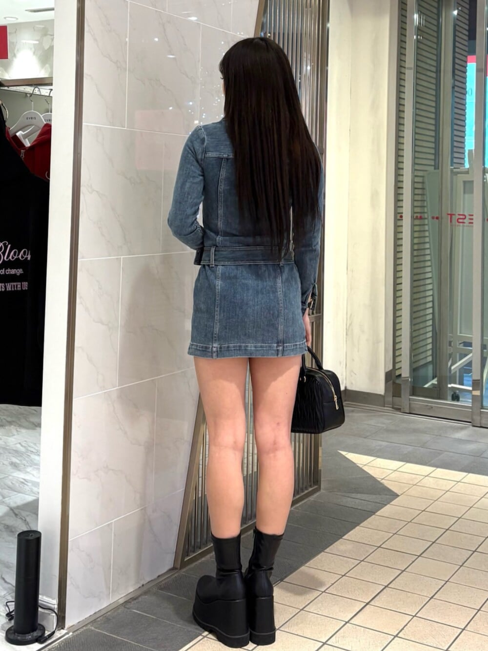 ブラック系のハンドバッグ、ブルー系のワンピース、ブラック系のブーツを着用したレディースの冬コーディネートの3枚目の写真