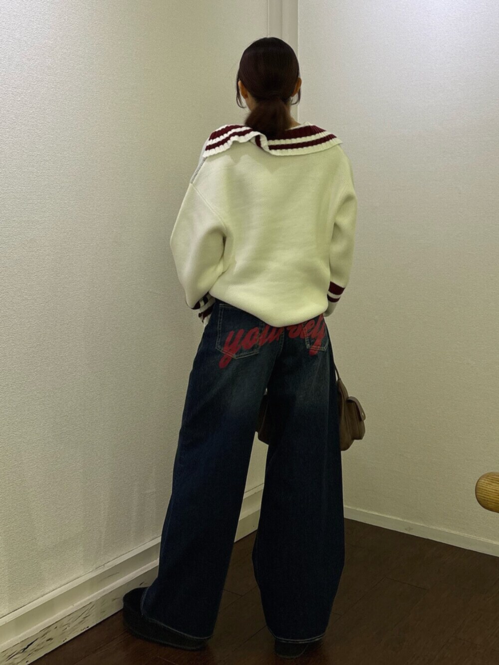 ブルー系のデニムパンツ、ブラウン系のハンドバッグ、ホワイト系のニット/セーターを着用したレディースの冬コーディネートの3枚目の写真