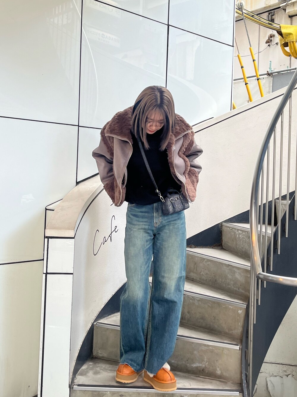 ブラウン系のムートンコート、ホワイト系のニット/セーター、ブルー系のデニムパンツを着用したレディースの冬コーディネートの4枚目の写真