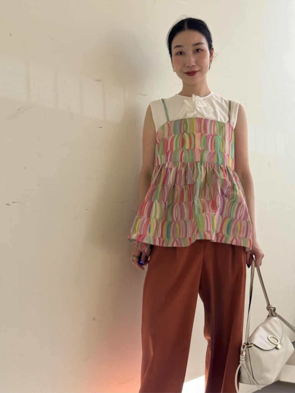 ホワイト系のキャミソール、ホワイト系のショルダーバッグ、イエロー系のスラックスを着用したレディースの夏コーディネートの3枚目の写真