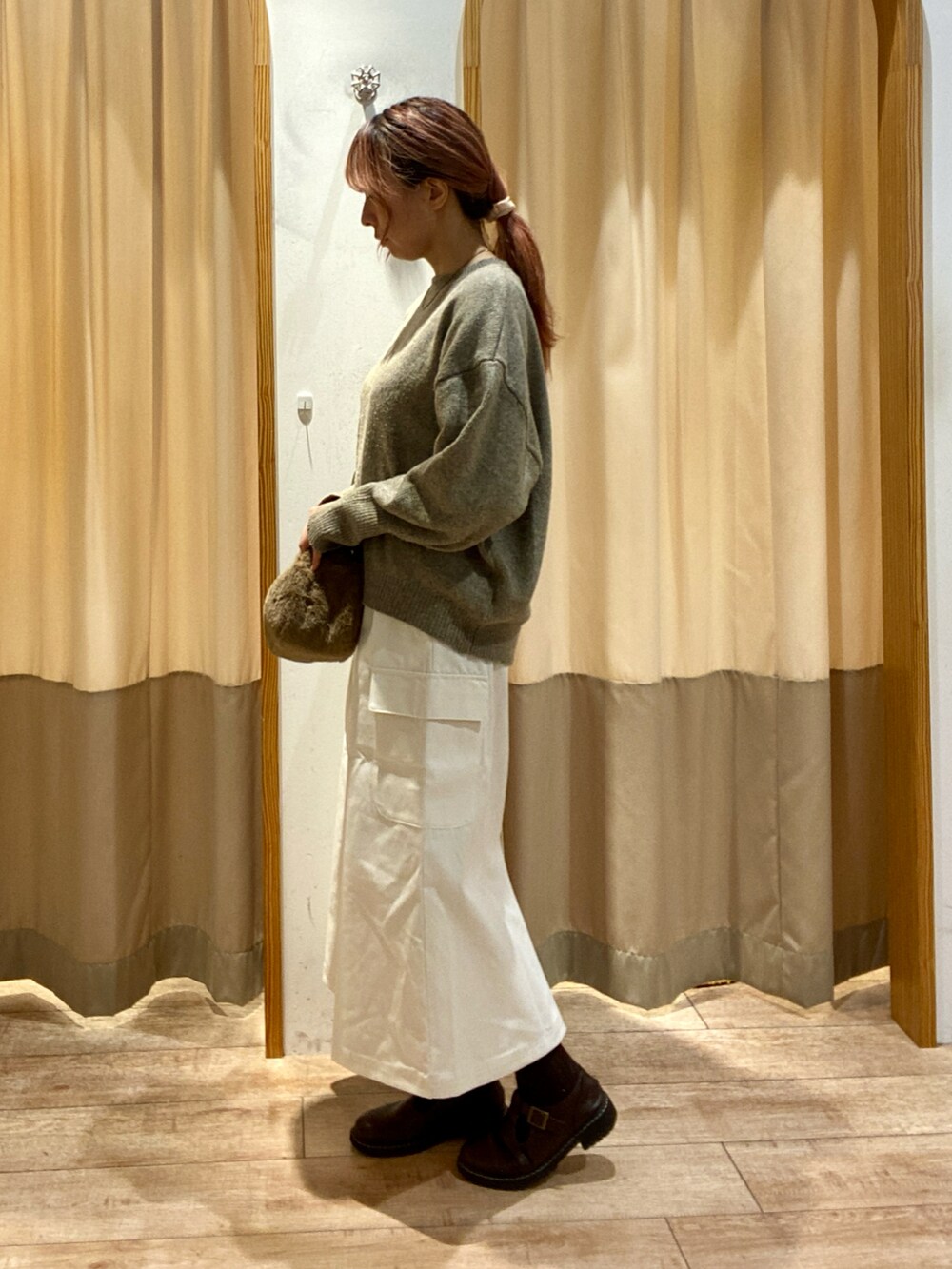 ブラウン系のニット/セーター、ブラウン系のハンドバッグ、ホワイト系のスカートを着用したレディースの秋コーディネートの2枚目の写真