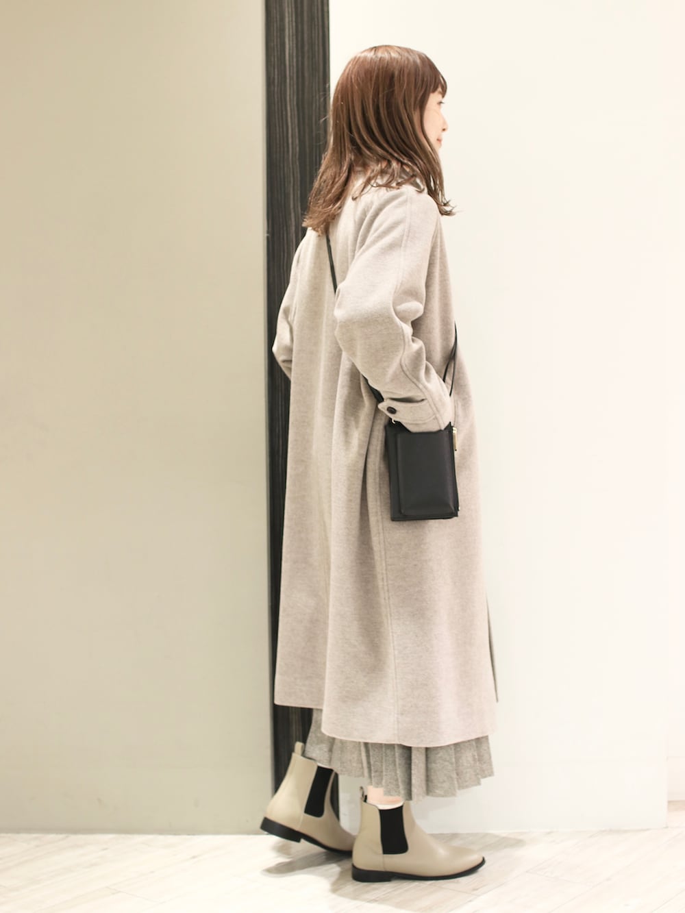 グレー系のステンカラーコート、グリーン系のニット/セーター、ベージュ系のスカートを着用したレディースの冬コーディネートの3枚目の写真