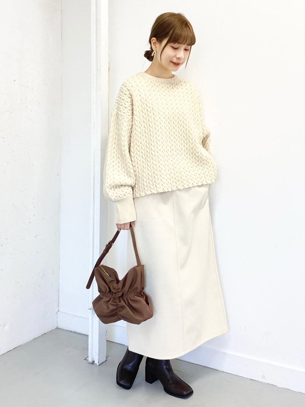 ブラウン系のハンドバッグ、ベージュ系のニット/セーター、ホワイト系のスカートを着用したレディースの冬コーディネートの2枚目の写真
