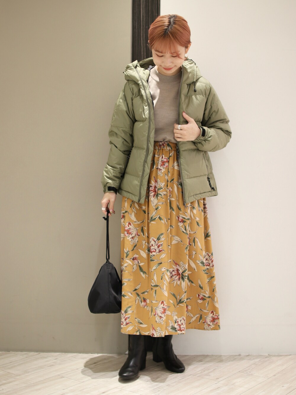 グリーン系のダウンジャケット/コート、ベージュ系のニット/セーター、オレンジ系のスカートを着用したレディースの冬コーディネートの2枚目の写真