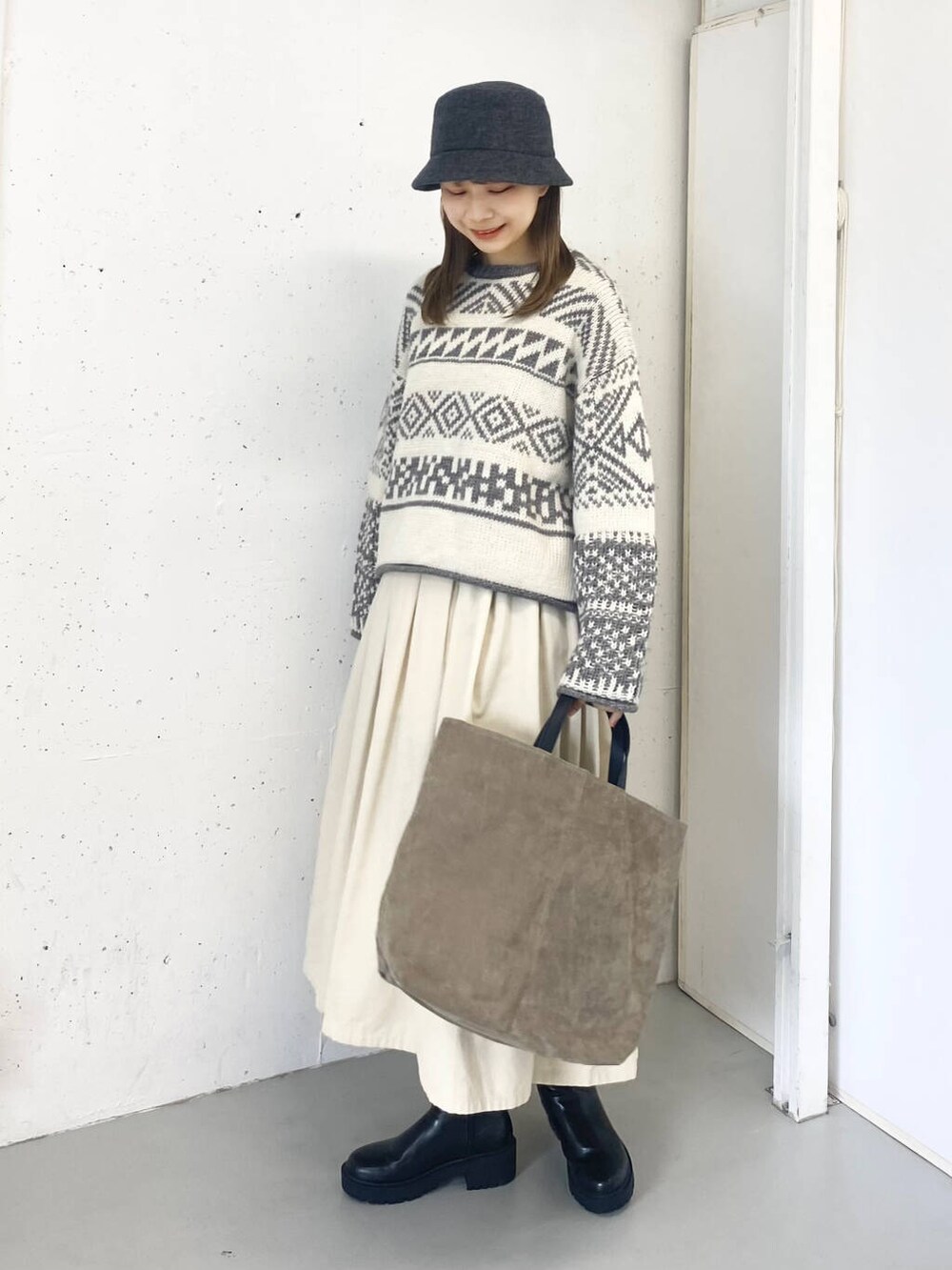 ベージュ系のトートバッグ、ブラック系のブーツ、ホワイト系のスカートを着用したレディースの秋コーディネートの2枚目の写真