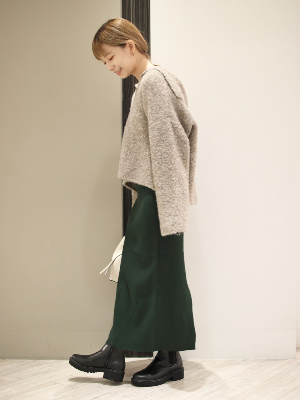 ホワイト系のトートバッグ、ブラック系のブーツ、グリーン系のスカートを着用したレディースの秋コーディネートの3枚目の写真