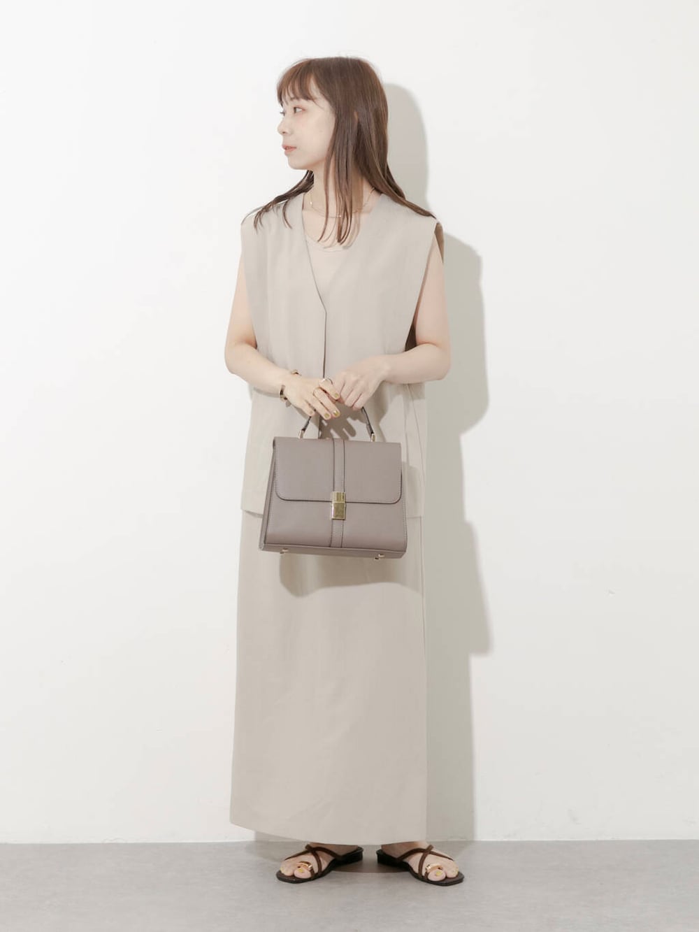 グレー系のハンドバッグ、ブラウン系のサンダル、ベージュ系のワンピースを着用したレディースの夏コーディネートの4枚目の写真
