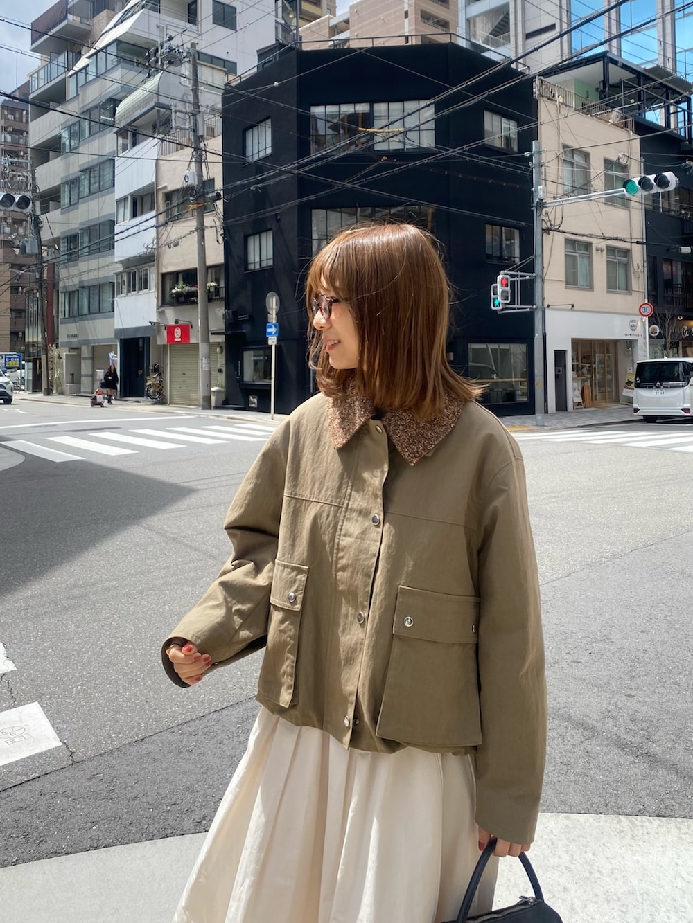 グリーン系のブルゾン、ホワイト系のスカート、ブラウン系のメガネを着用したレディースの春コーディネートの4枚目の写真