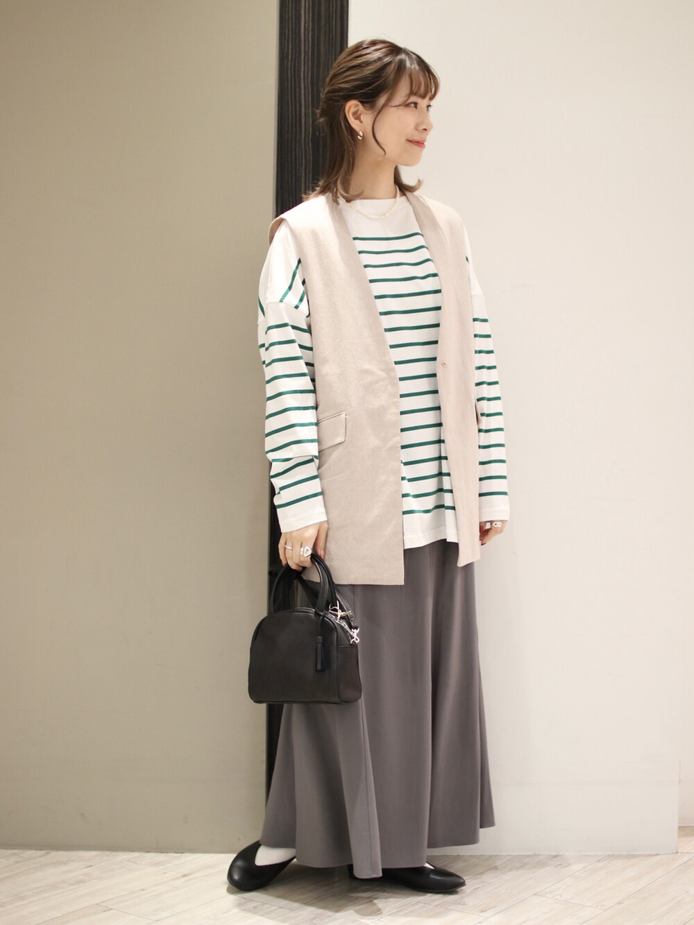 ブラック系のボストンバッグ、グリーン系のTシャツ/カットソー、グレー系のスカートを着用したレディースの春コーディネートの3枚目の写真