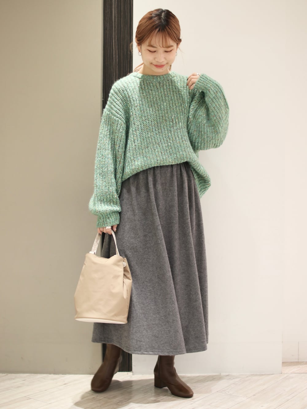 グリーン系のニット/セーター、グレー系のスカート、ベージュ系のショルダーバッグを着用したレディースの冬コーディネートの2枚目の写真