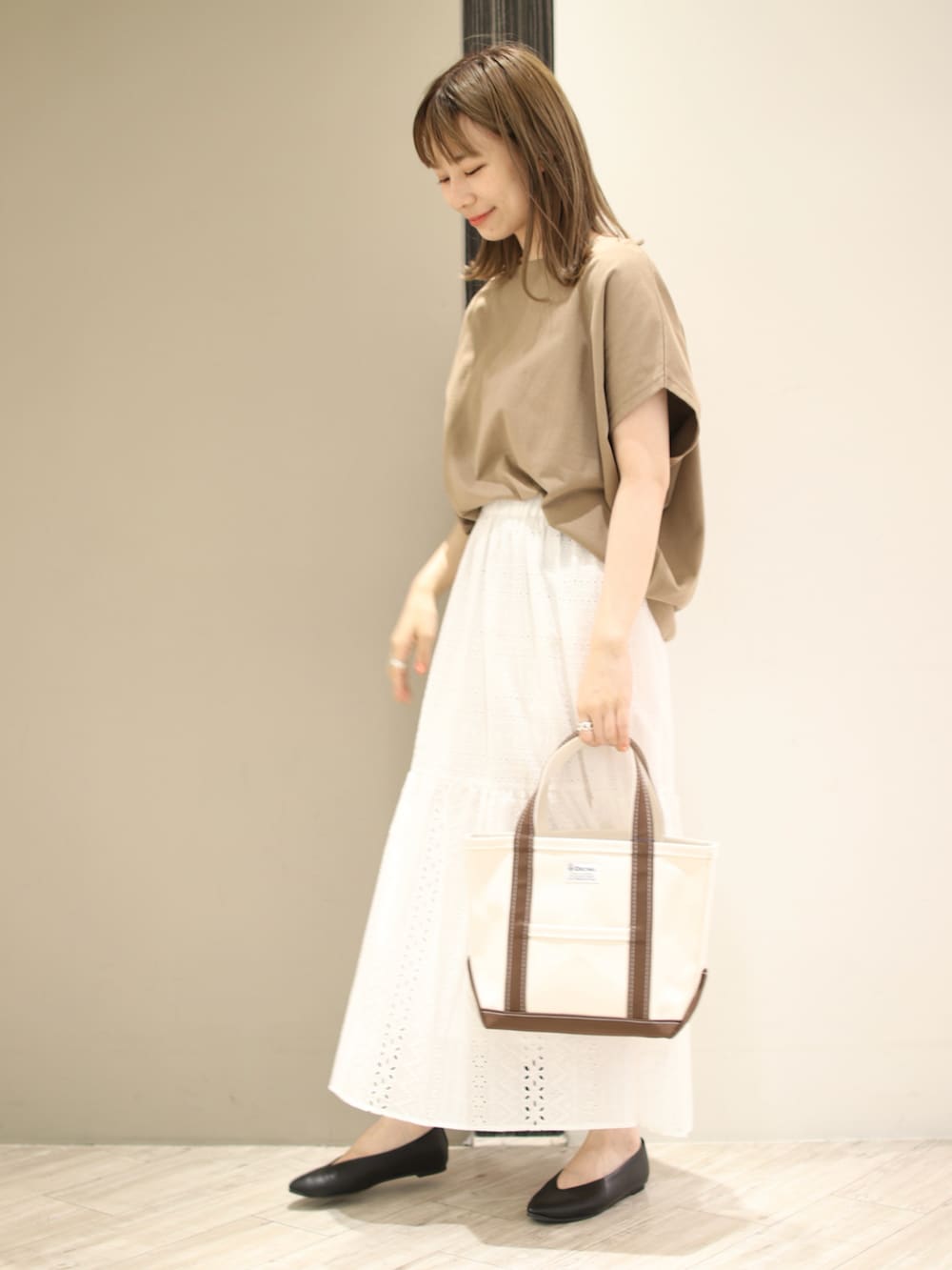 ブラウン系のトートバッグ、ベージュ系のTシャツ/カットソー、ホワイト系のスカートを着用したレディースの夏コーディネートの4枚目の写真