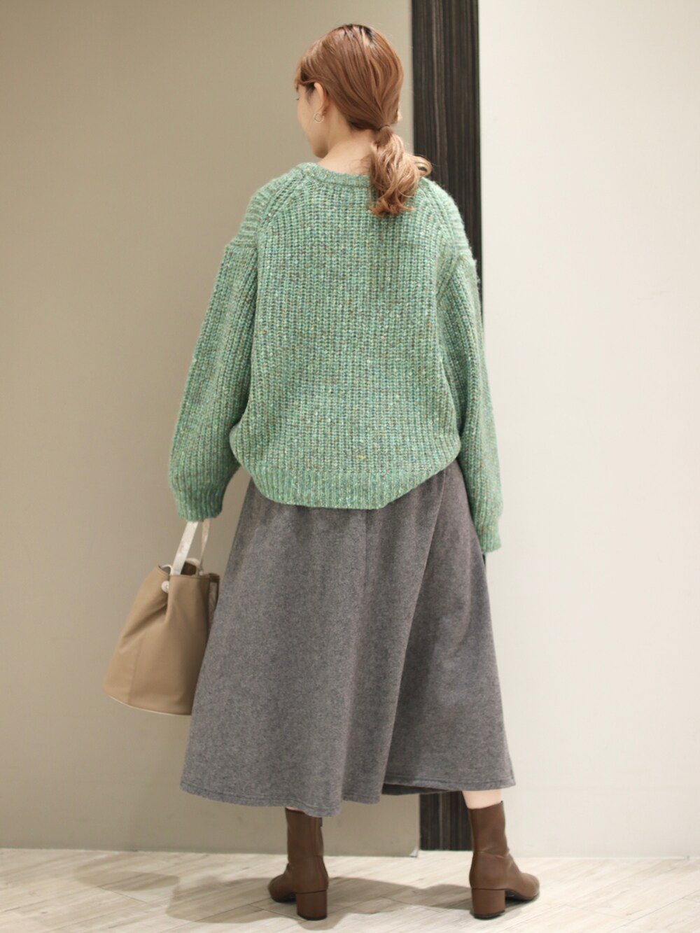 グリーン系のニット/セーター、グレー系のスカート、ベージュ系のショルダーバッグを着用したレディースの冬コーディネートの3枚目の写真