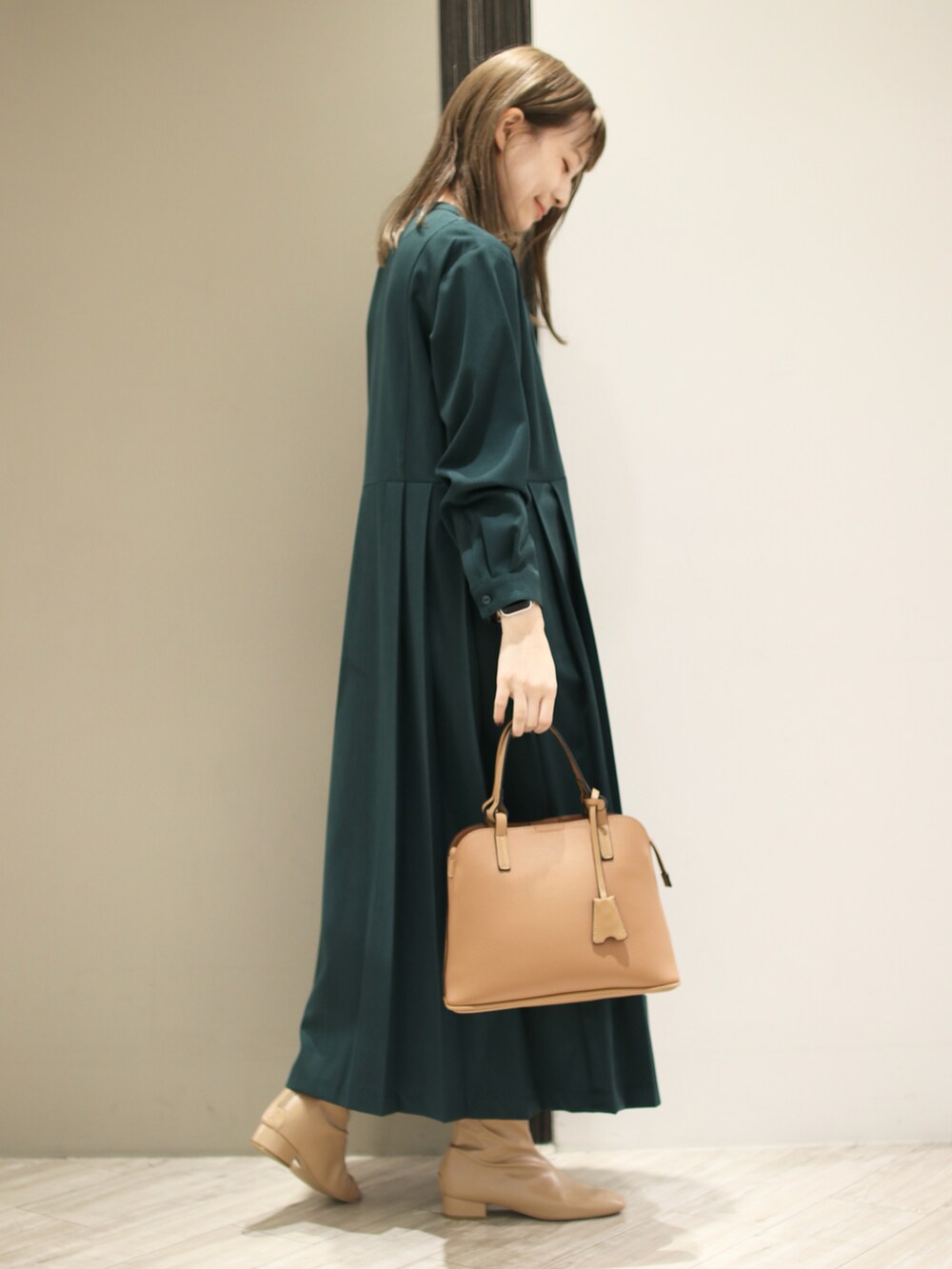 イエロー系のハンドバッグ、グリーン系のワンピース、ベージュ系のブーツを着用したレディースの秋コーディネートの2枚目の写真