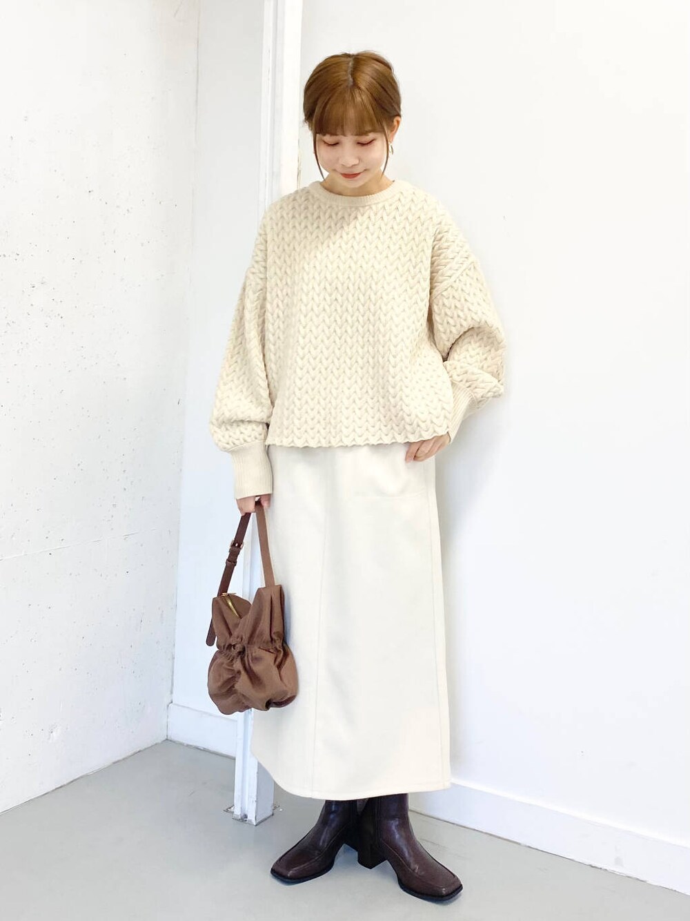 ブラウン系のハンドバッグ、ブラウン系のブーツ、ホワイト系のスカートを着用したレディースの冬コーディネートの3枚目の写真