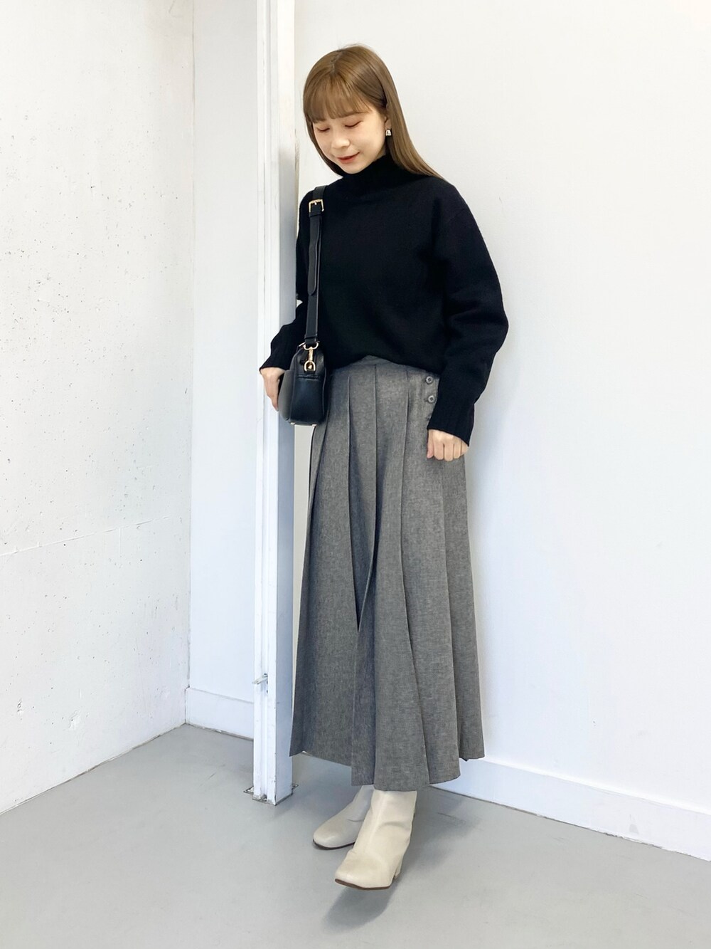 グレー系のスカート、ホワイト系のブーツ、ブラック系のショルダーバッグを着用したレディースの冬コーディネートの3枚目の写真