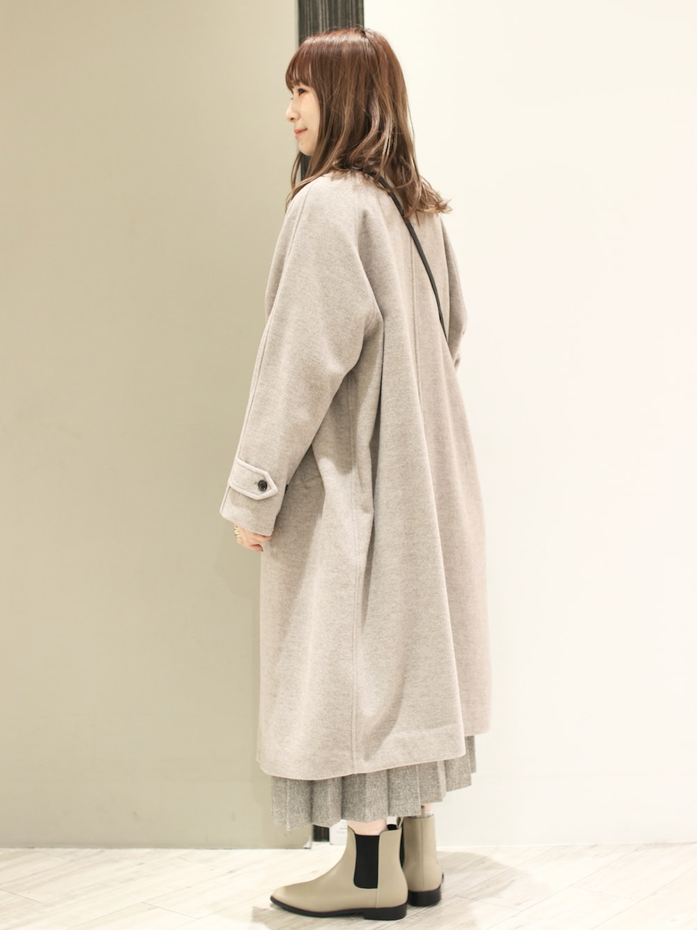 グレー系のステンカラーコート、グリーン系のニット/セーター、ベージュ系のスカートを着用したレディースの冬コーディネートの4枚目の写真