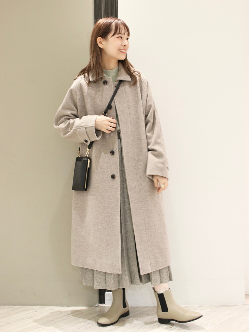 グレー系のステンカラーコート、グリーン系のニット/セーター、ベージュ系のスカートを着用したレディースの冬コーディネートの2枚目の写真