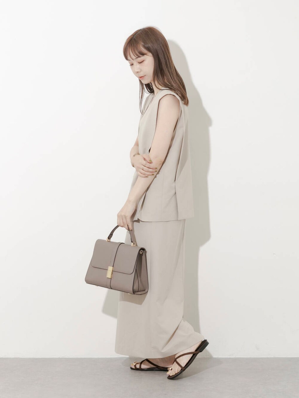 グレー系のハンドバッグ、ブラウン系のサンダル、ベージュ系のワンピースを着用したレディースの夏コーディネートの5枚目の写真