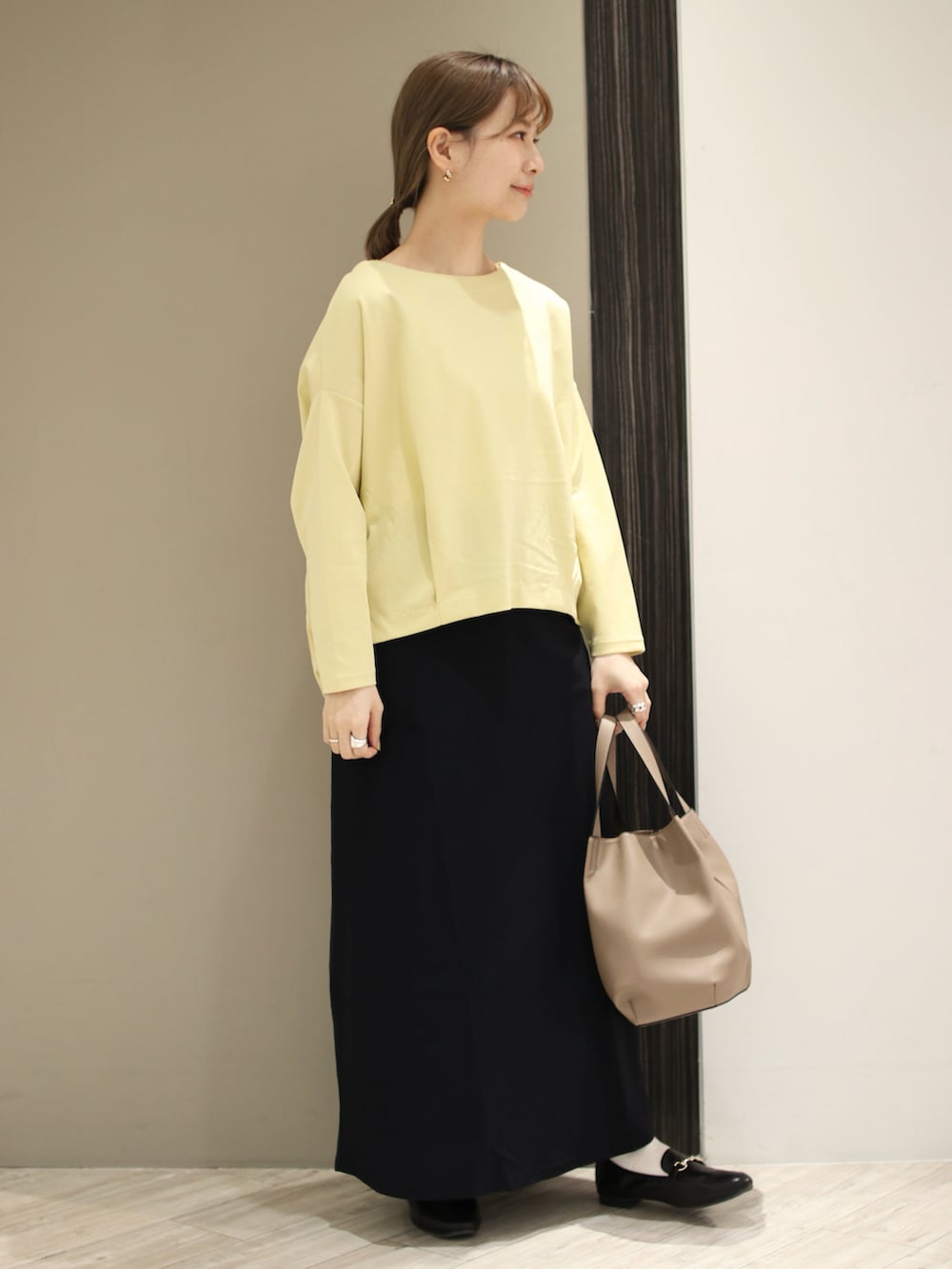 ベージュ系のトートバッグ、イエロー系のTシャツ/カットソー、ブルー系のスカートを着用したレディースの冬コーディネートの2枚目の写真