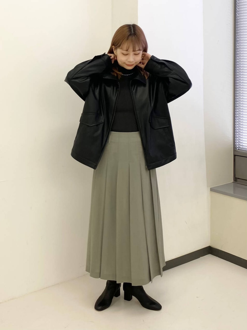 グレー系のスカート、グリーン系のニット/セーター、ブラック系のブルゾンを着用したレディースの秋コーディネートの2枚目の写真