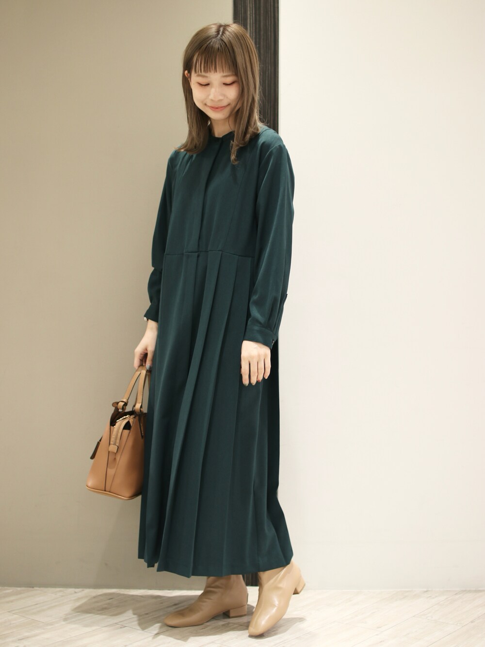 イエロー系のハンドバッグ、グリーン系のワンピース、ベージュ系のブーツを着用したレディースの秋コーディネートの4枚目の写真