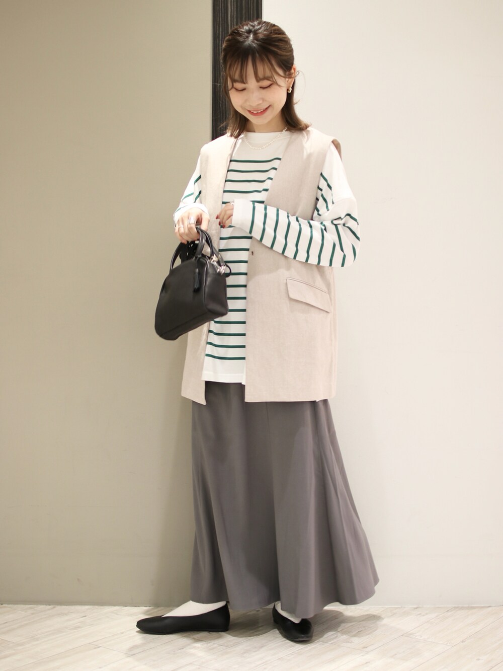 ブラック系のボストンバッグ、グリーン系のTシャツ/カットソー、グレー系のスカートを着用したレディースの春コーディネートの2枚目の写真