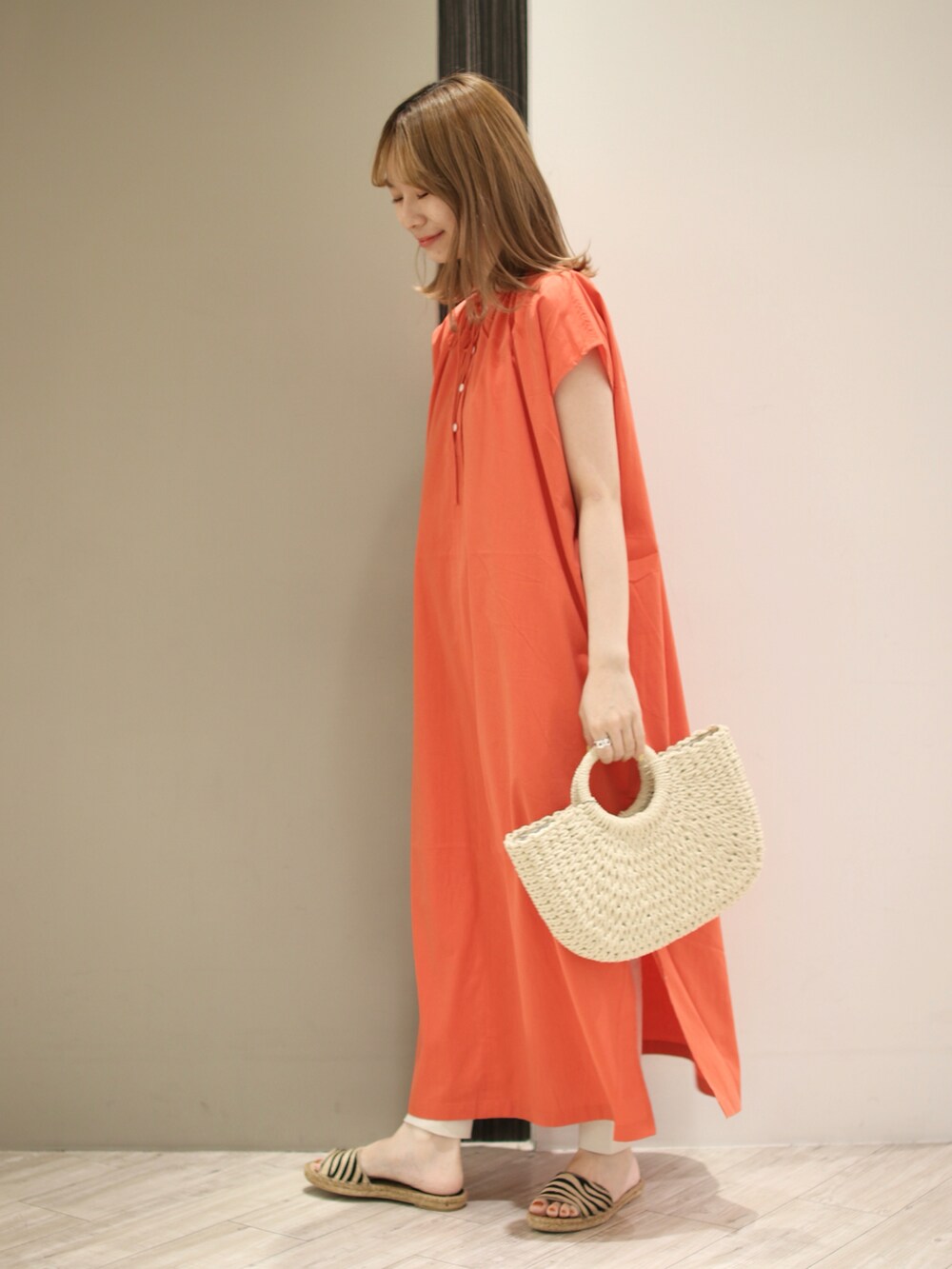 オレンジ系のワンピース、ホワイト系のハンドバッグ、ベージュ系のサンダルを着用したレディースの夏コーディネートの2枚目の写真