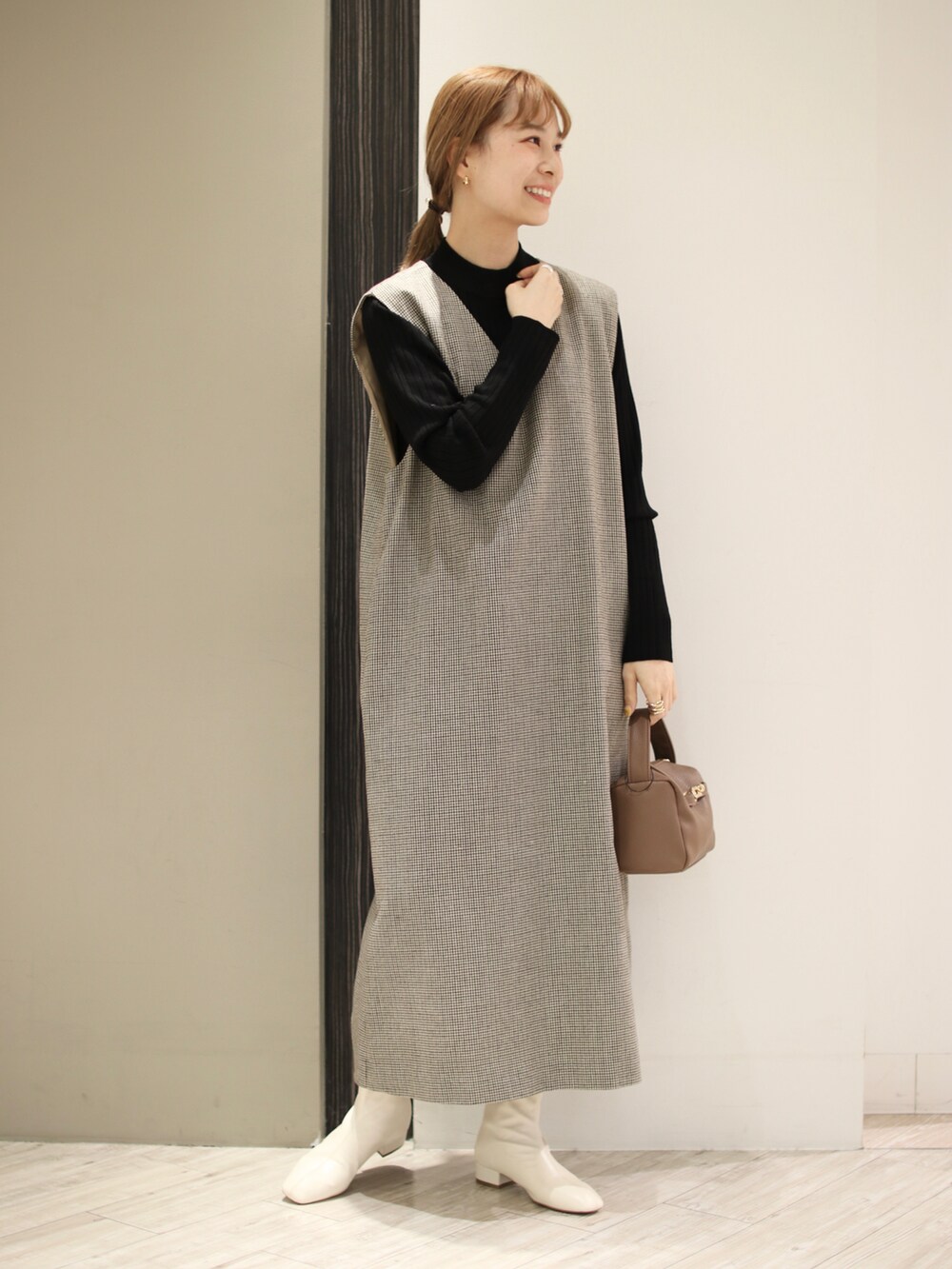 ブラウン系のハンドバッグ、ホワイト系のブーツ、ベージュ系のワンピースを着用したレディースの冬コーディネートの2枚目の写真
