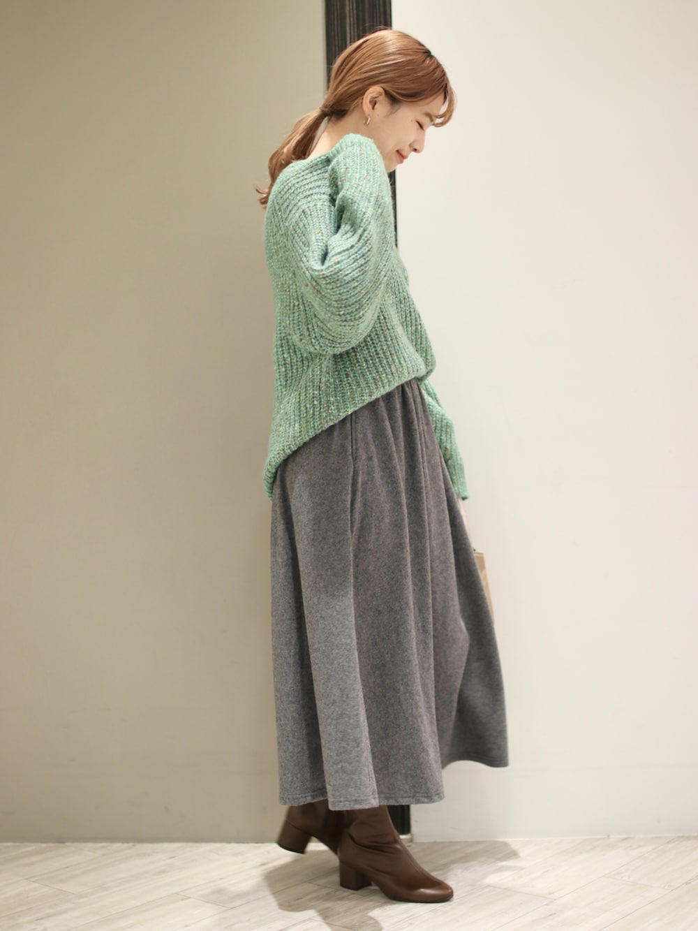グリーン系のニット/セーター、グレー系のスカート、ベージュ系のショルダーバッグを着用したレディースの冬コーディネートの4枚目の写真