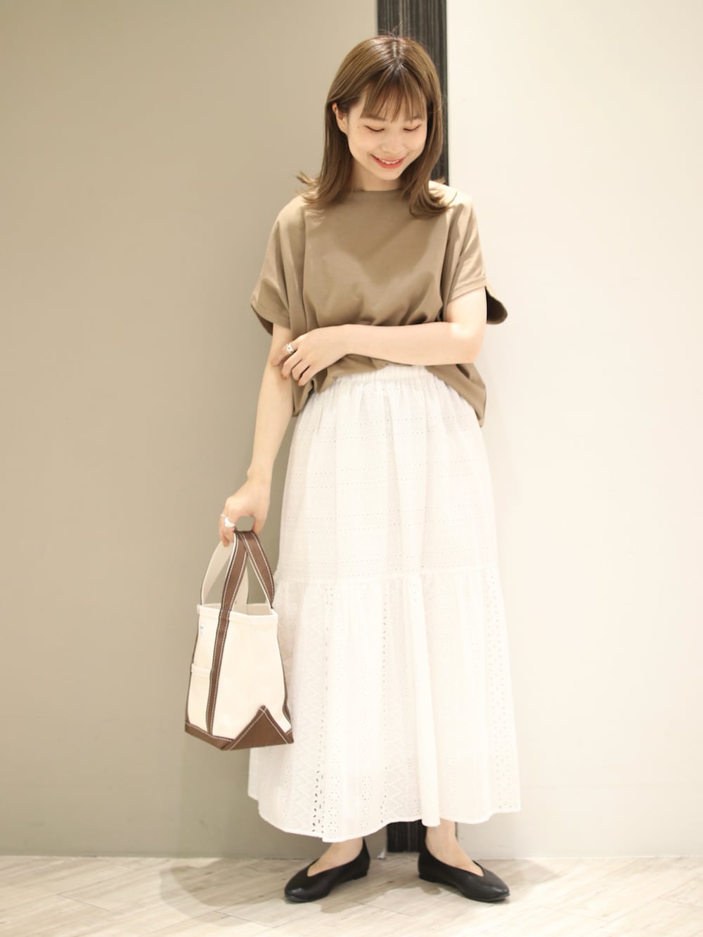 ブラウン系のトートバッグ、ベージュ系のTシャツ/カットソー、ホワイト系のスカートを着用したレディースの夏コーディネートの2枚目の写真
