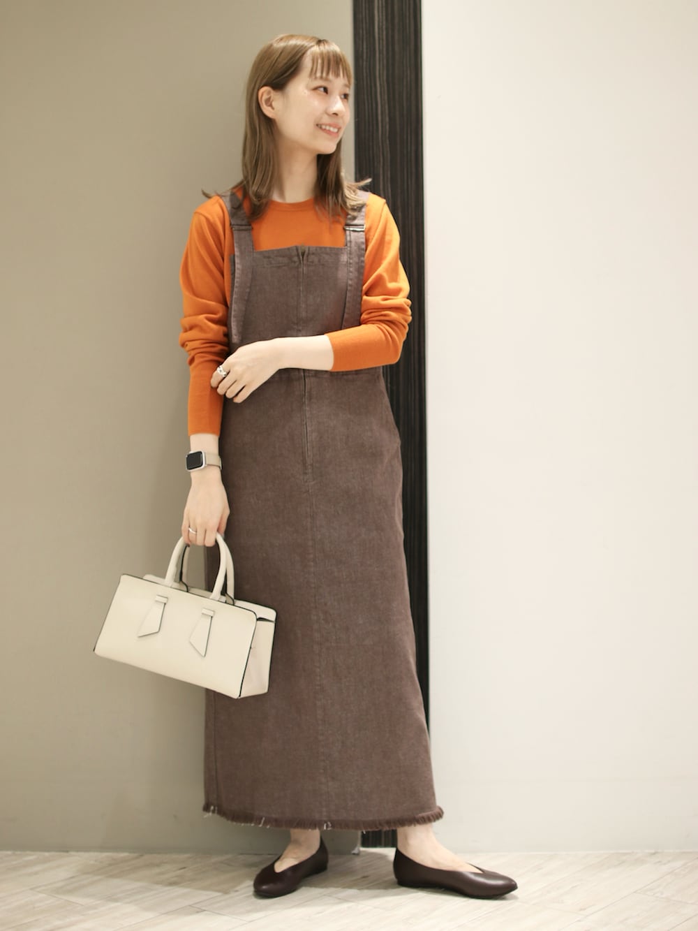 グレー系のトートバッグ、ブラウン系のサロペット/オーバーオール、オレンジ系のニット/セーターを着用したレディースの秋コーディネートの3枚目の写真