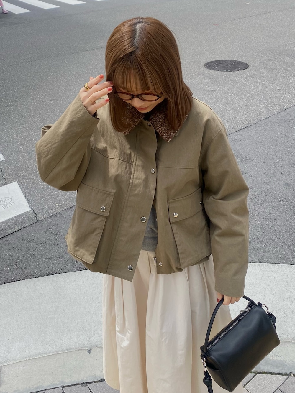 グリーン系のブルゾン、ホワイト系のスカート、ブラウン系のメガネを着用したレディースの春コーディネートの3枚目の写真