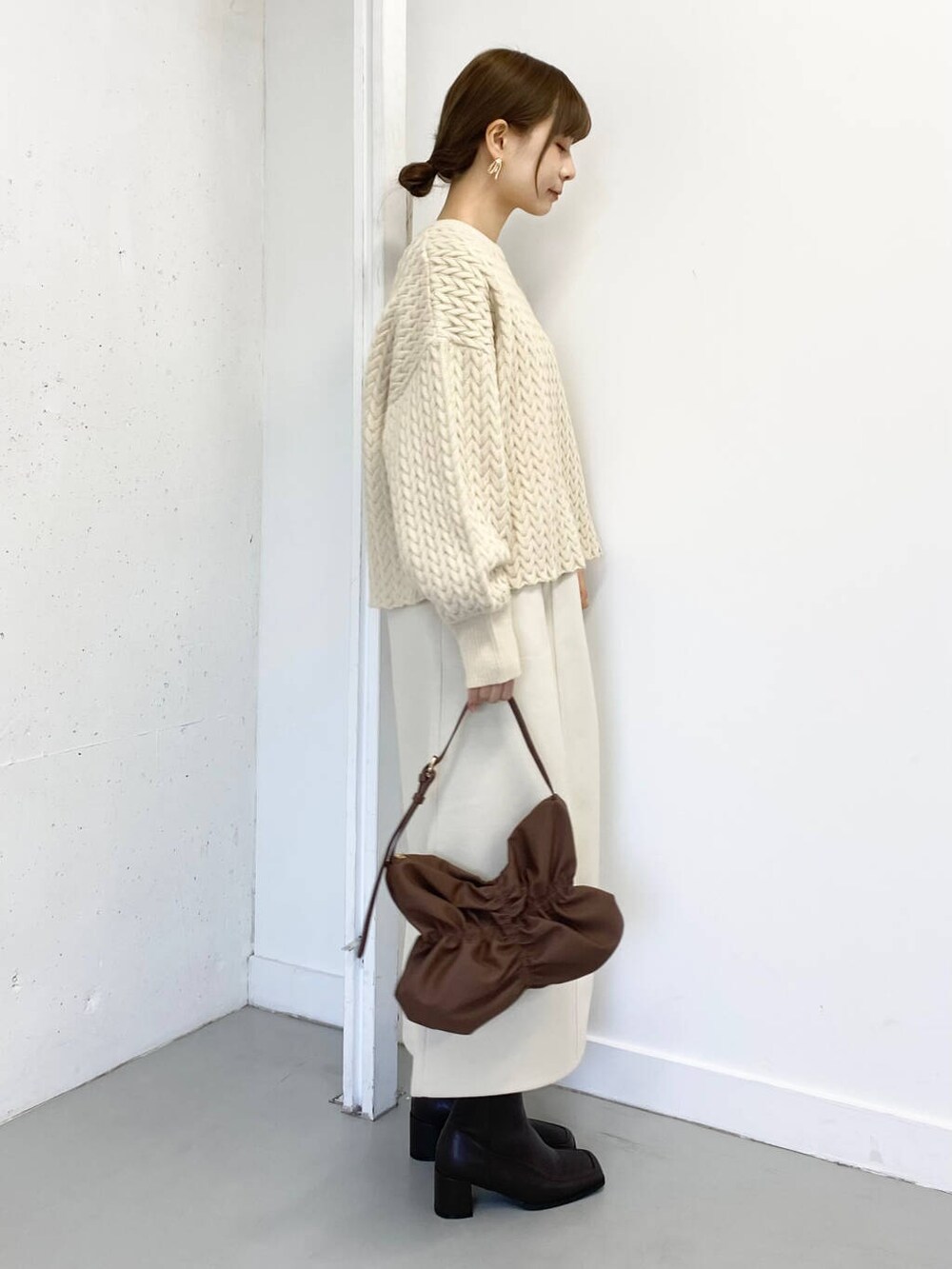 ブラウン系のハンドバッグ、ブラウン系のブーツ、ホワイト系のスカートを着用したレディースの冬コーディネートの2枚目の写真