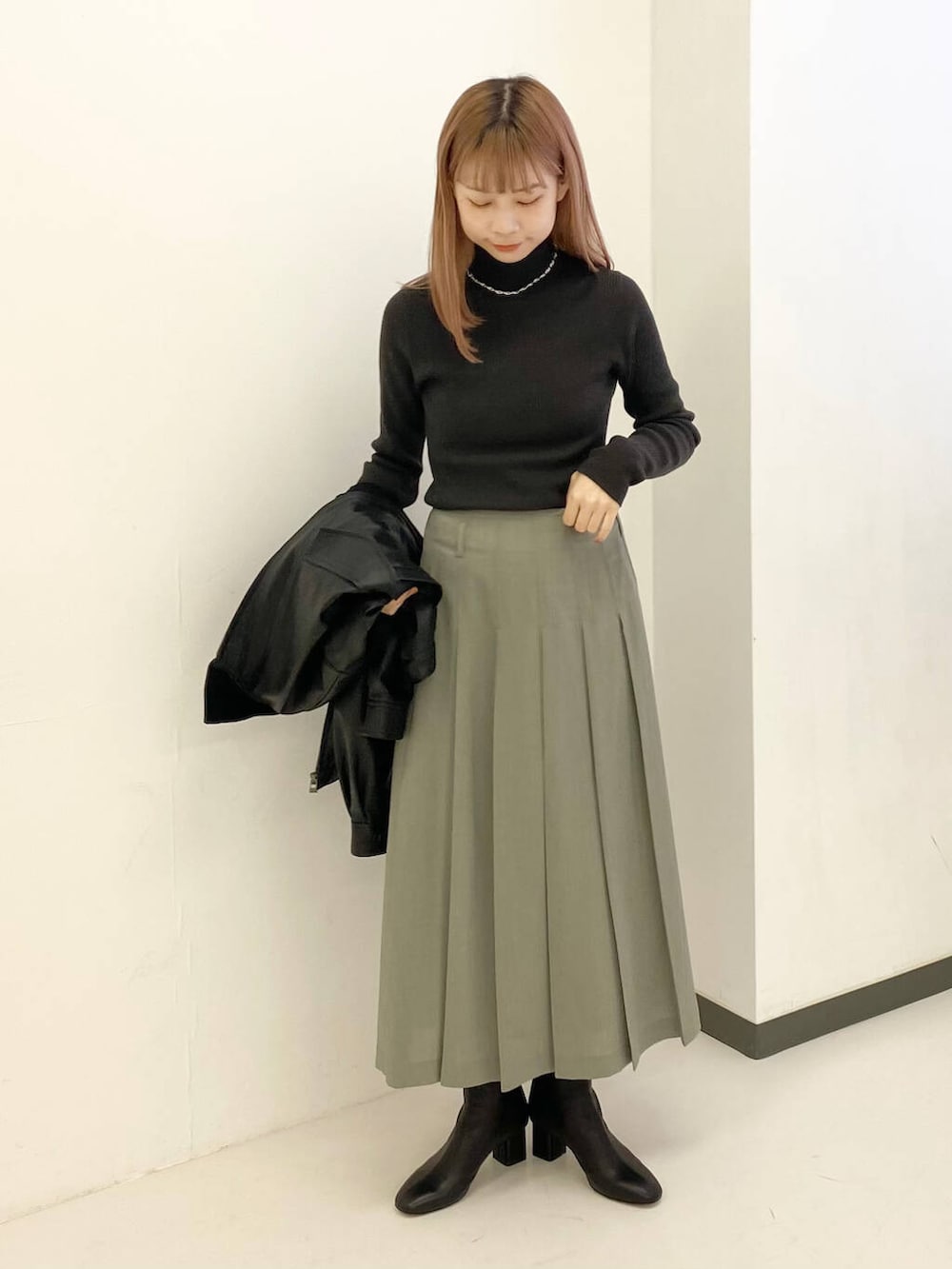 グレー系のスカート、グリーン系のニット/セーター、ブラック系のブルゾンを着用したレディースの秋コーディネートの4枚目の写真