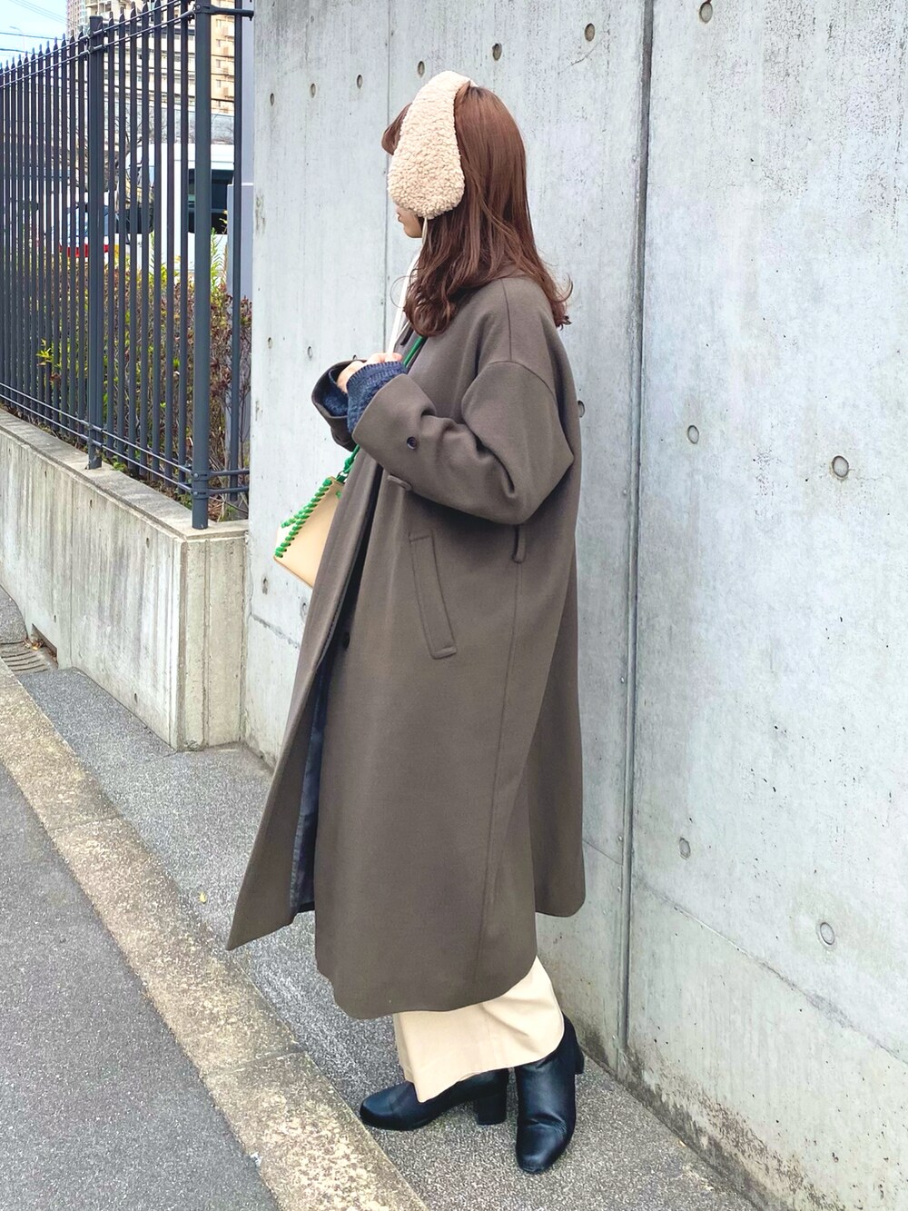グレー系のステンカラーコート、グリーン系のショルダーバッグ、ブラック系のブーツを着用したレディースの冬コーディネートの3枚目の写真