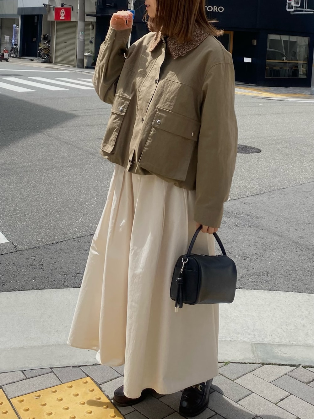 グリーン系のブルゾン、ホワイト系のスカート、ブラウン系のメガネを着用したレディースの春コーディネートの2枚目の写真