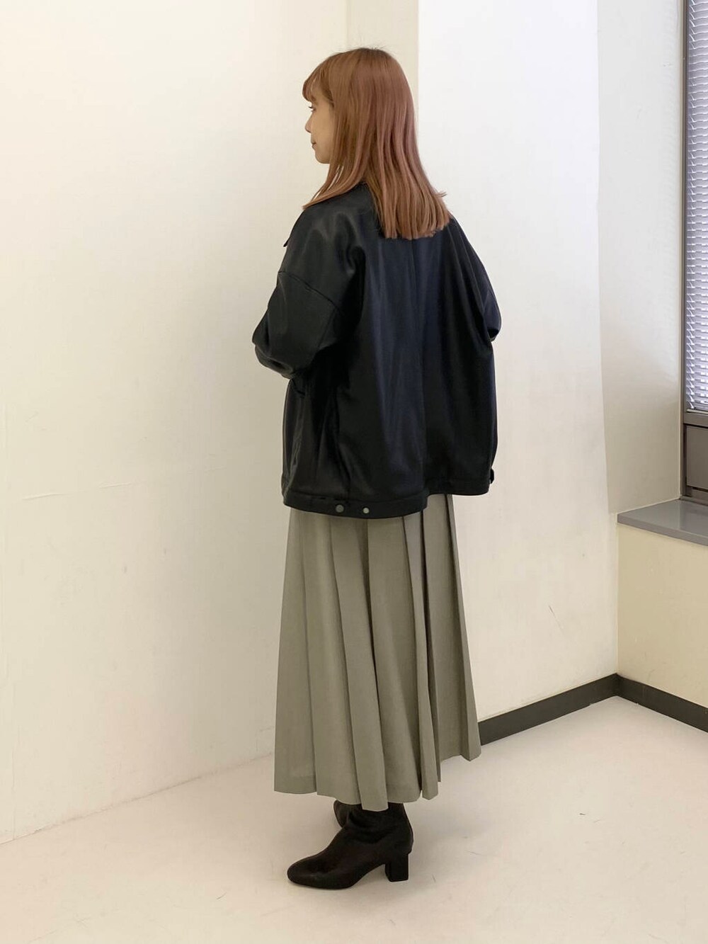 グレー系のスカート、グリーン系のニット/セーター、ブラック系のブルゾンを着用したレディースの秋コーディネートの3枚目の写真