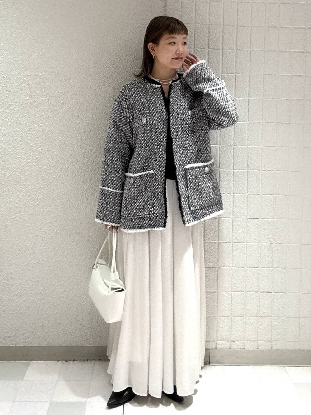 ホワイト系のスカート、ブラック系のノーカラージャケット、ホワイト系のショルダーバッグを着用したレディースの春コーディネートの2枚目の写真