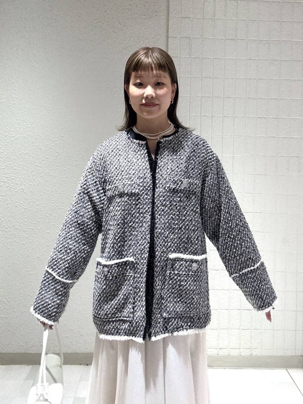 ホワイト系のスカート、ブラック系のノーカラージャケット、ホワイト系のショルダーバッグを着用したレディースの春コーディネートの6枚目の写真