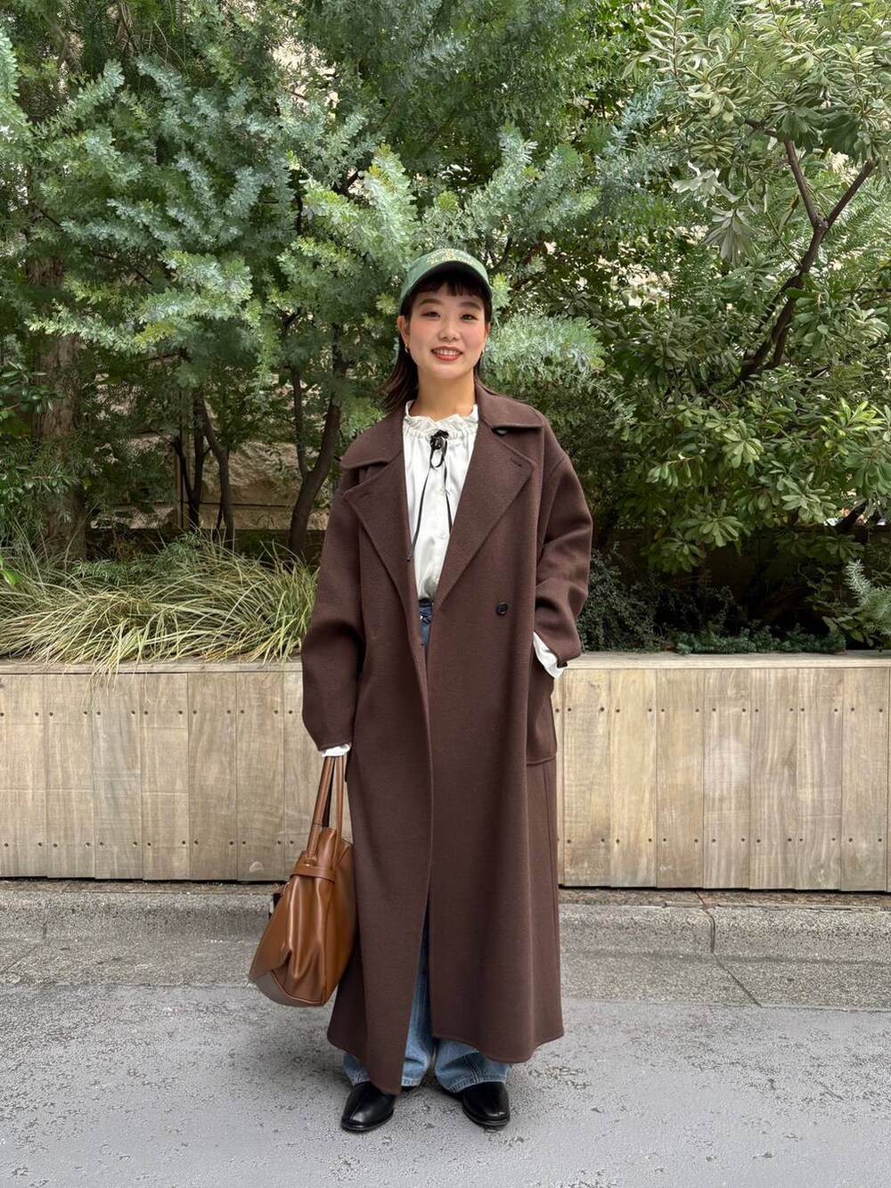 ブラウン系のステンカラーコート、ブルー系のデニムパンツ、ホワイト系のシャツ/ブラウスを着用したレディースの秋コーディネートの2枚目の写真