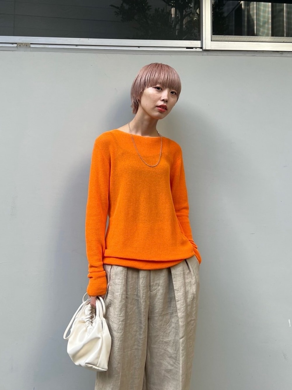 オレンジ系のニット/セーター、ベージュ系のスラックス、ホワイト系のショルダーバッグを着用したレディースの冬コーディネートの2枚目の写真