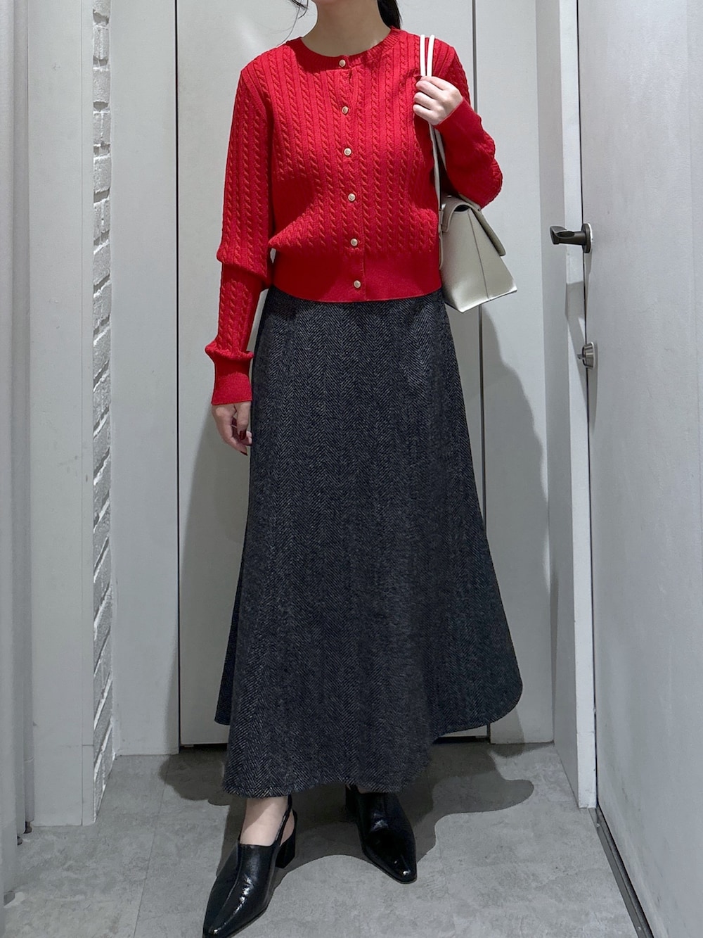 ブラック系のスカート、ホワイト系のショルダーバッグ、レッド系のニット/セーターを着用したレディースの冬コーディネートの2枚目の写真