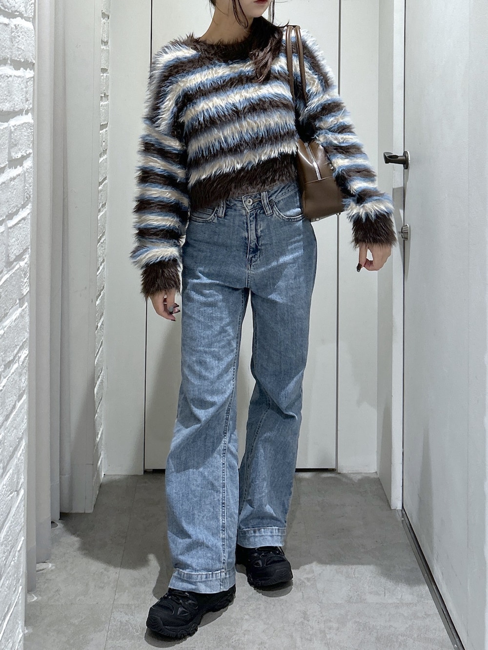 ブルー系のデニムパンツ、ブラウン系のトートバッグ、ブラウン系のニット/セーターを着用したレディースの秋コーディネートの2枚目の写真