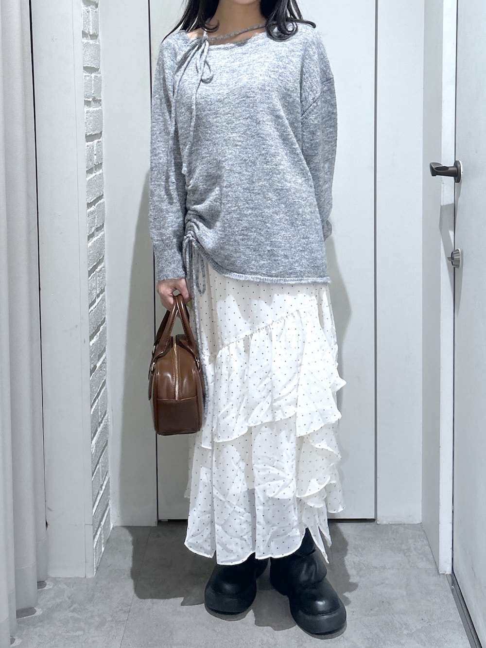 グレー系のニット/セーター、ブラウン系のハンドバッグ、ホワイト系のスカートを着用したレディースの春コーディネートの4枚目の写真