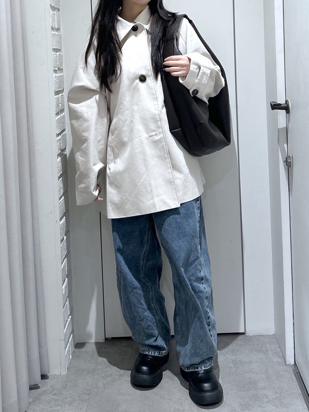 ブラウン系のトートバッグ、ホワイト系のニット/セーター、ブルー系のデニムパンツを着用したレディースの春コーディネートの2枚目の写真