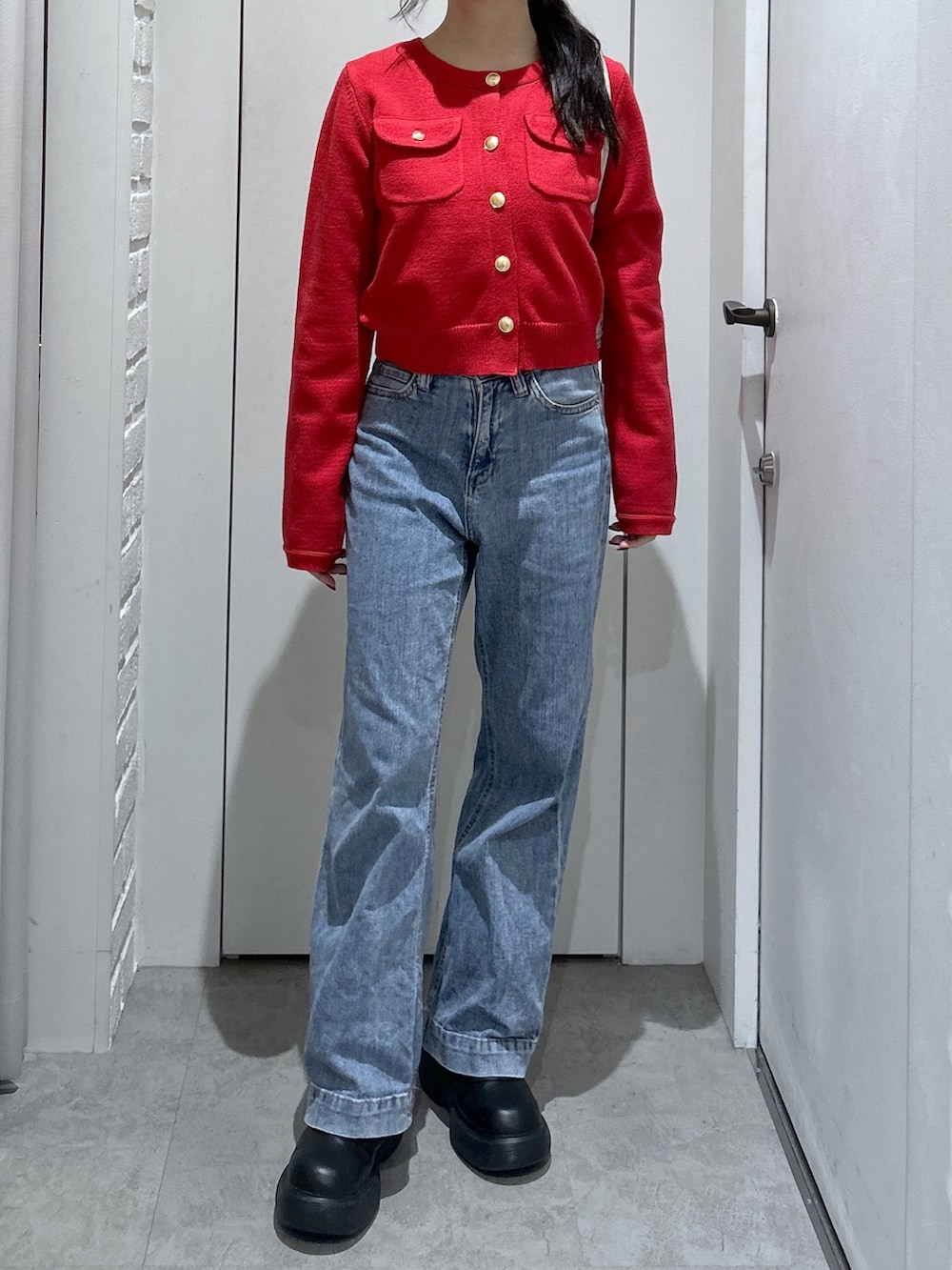 レッド系のニット/セーター、ブルー系のデニムパンツ、ホワイト系のショルダーバッグを着用したレディースの秋コーディネートの2枚目の写真