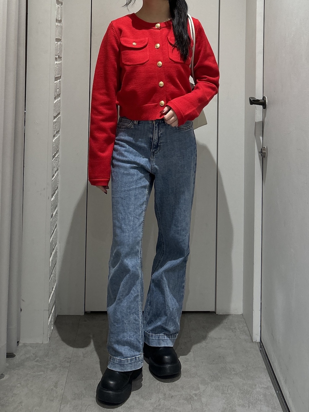 レッド系のニット/セーター、ブルー系のデニムパンツ、ホワイト系のショルダーバッグを着用したレディースの秋コーディネートの3枚目の写真