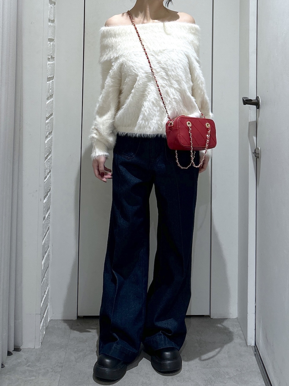 ブルー系のデニムパンツ、レッド系のショルダーバッグ、ホワイト系のニット/セーターを着用したレディースの冬コーディネートの2枚目の写真