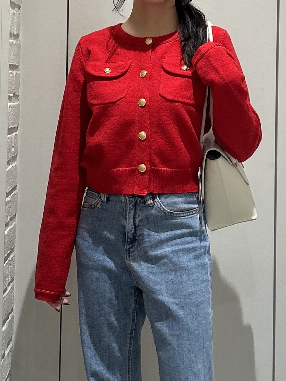 レッド系のニット/セーター、ブルー系のデニムパンツ、ホワイト系のショルダーバッグを着用したレディースの秋コーディネートの4枚目の写真